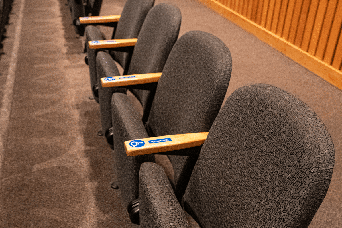 Auditorium seating shows the blue and white international symbol of access on the wooden arm rests