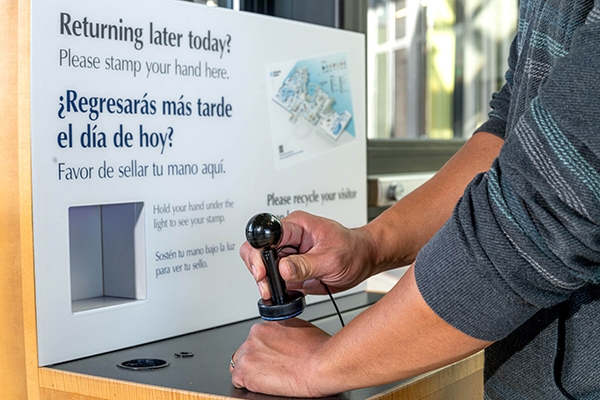 A guest gives themself a reentry handstamp near the Aquarium’s exit using a black handheld stamp