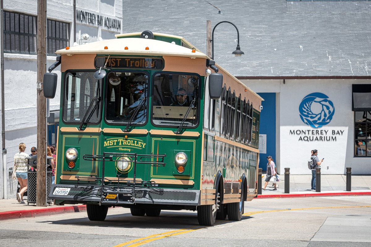 A front-end view of a green and brown trolley driving up a hill away from the Aquarium