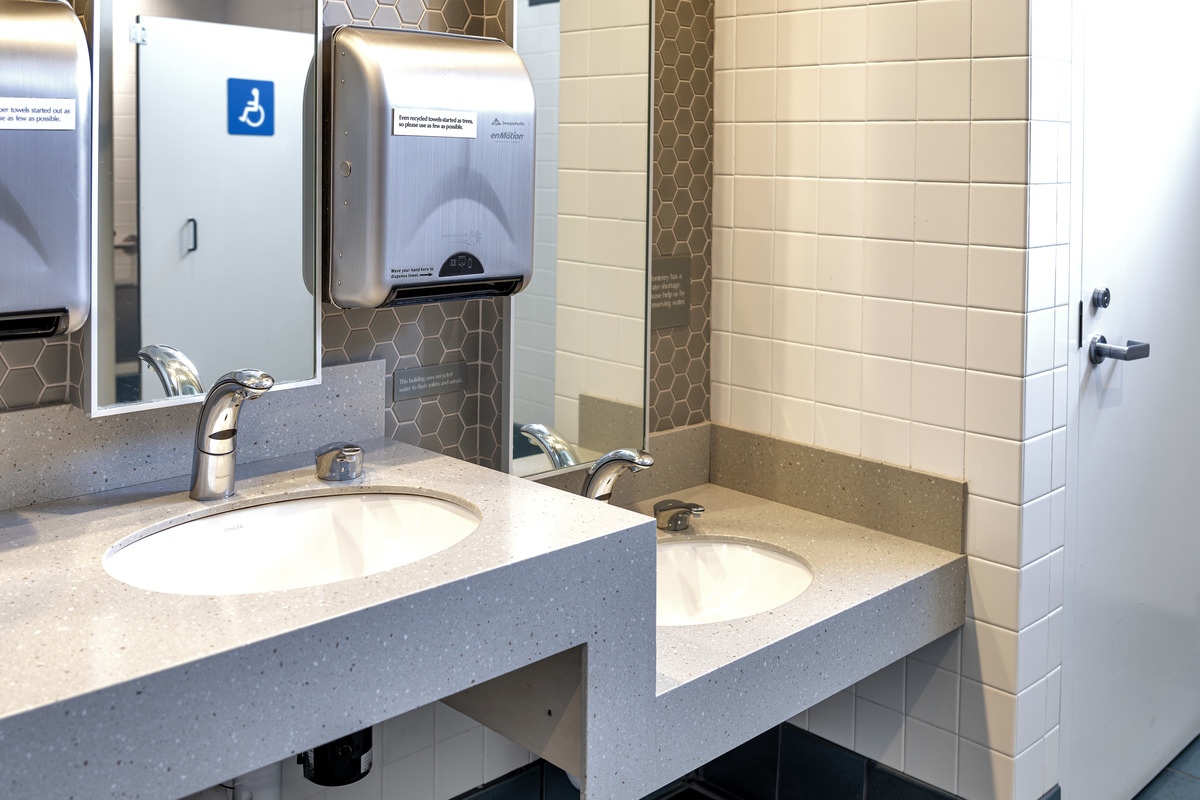 The interior of an Aquarium restroom, showcasing lowered sinks. Also present are two reflective vertical mirrors and two electronic paper towel dispensers