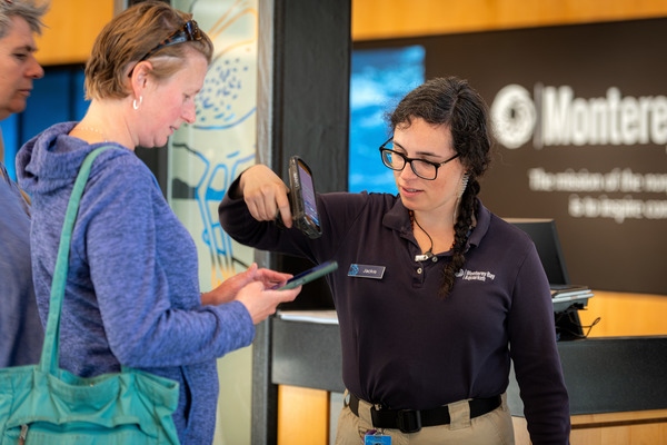 A member of the Monterey Bay Aquarium staff uses an electronic device to scan the digital tickets on a guests’ cell phone