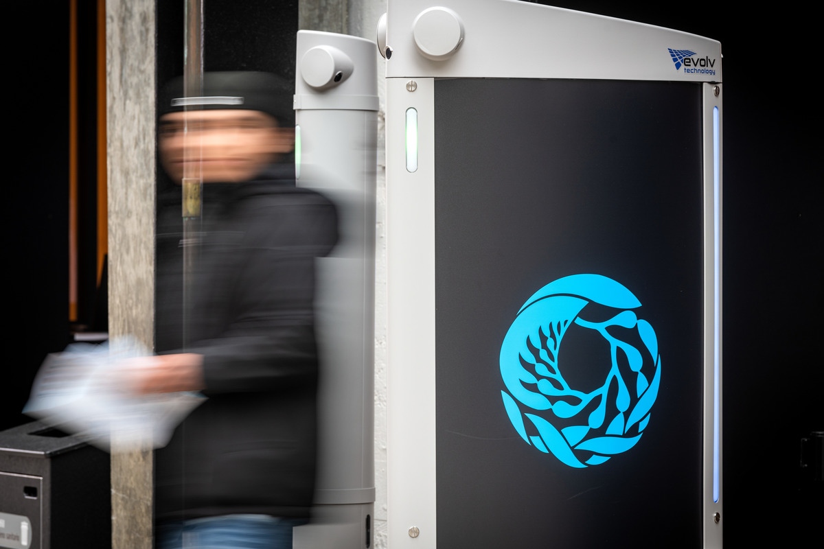 The blurred image of a person wearing a black jacket as they walk through a touchless security checkpoint with an blue Aquarium logo on the side