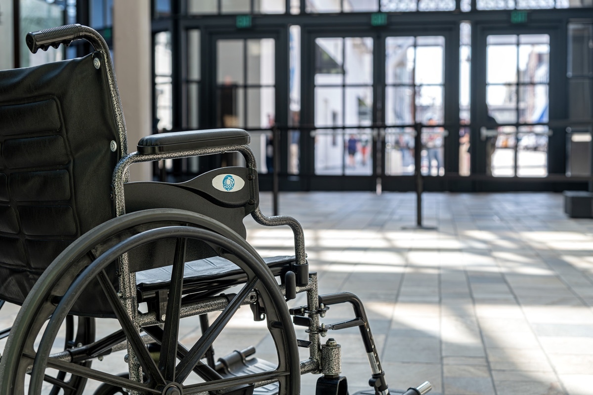 A manual wheelchair with the Monterey Bay Aquarium logo sits empty facing towards the entry doors of the Aquarium