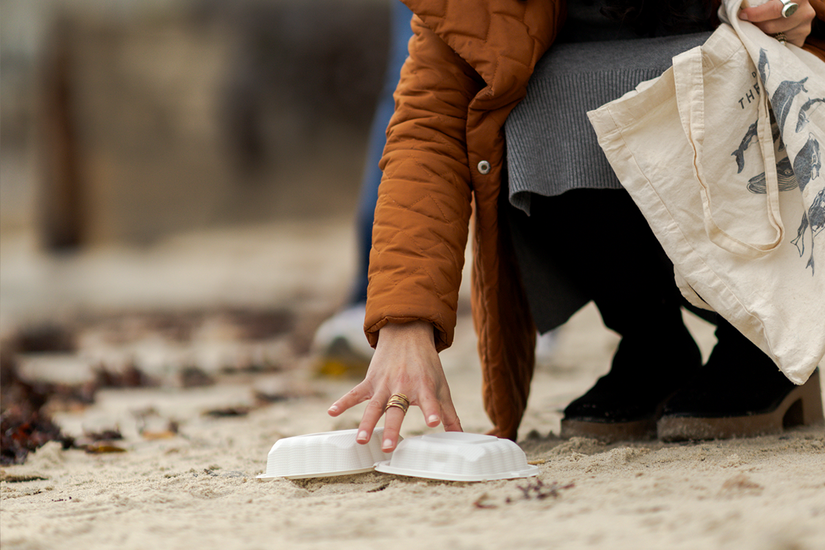 A hand picking up trash on the beach and placing in a reusable bag