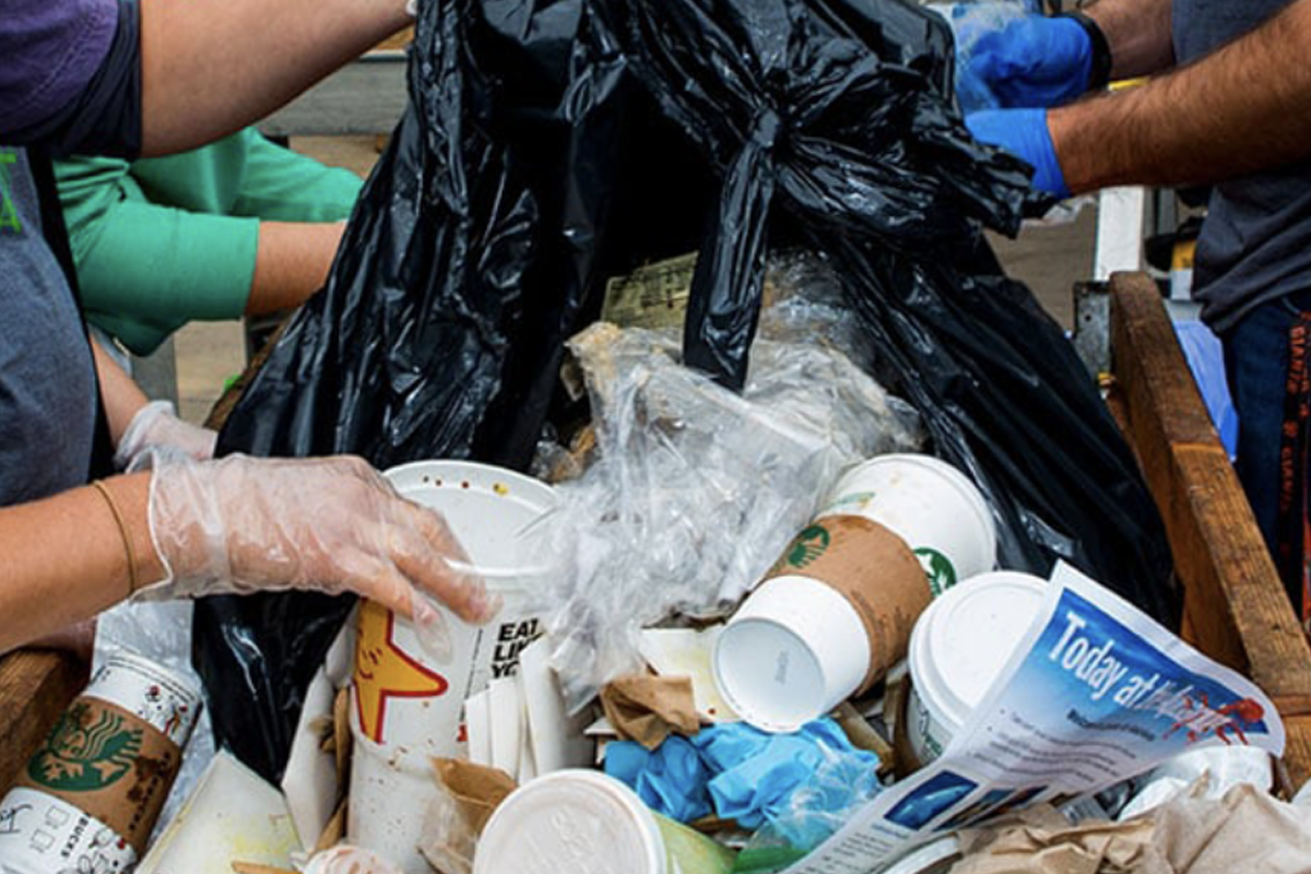 People wearing gloves sorting trash with disposable cups and plastic waste into a garbage bag
