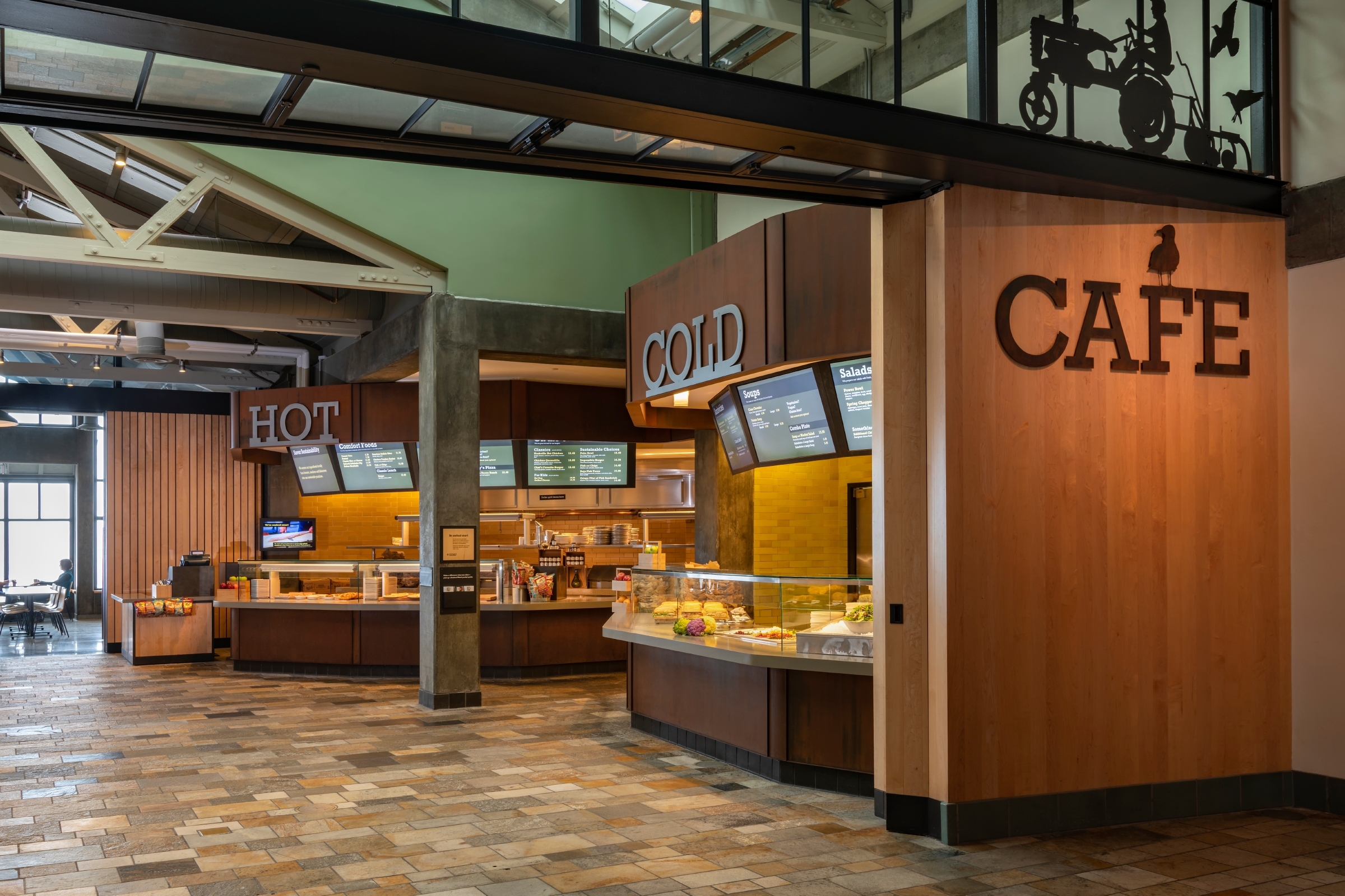 Monterey Bay Aquarium cafe interior with separate hot and cold counters, digital menu boards, food displays, and a cafe sign on a wooden wall