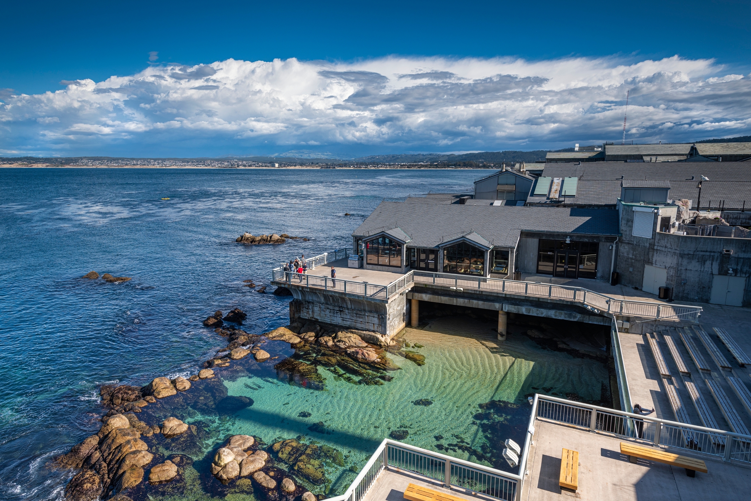 Aerial show of the backdeck of the Aquarium overlooking the Pacific Ocean on a sunny day with white clouds in the sky