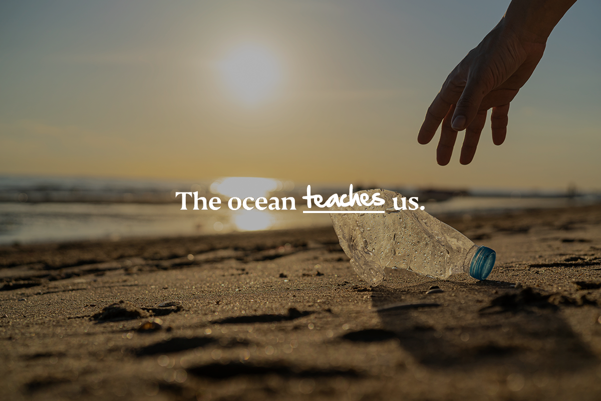 A hand picking up a plastic water bottle on the beach at sunset