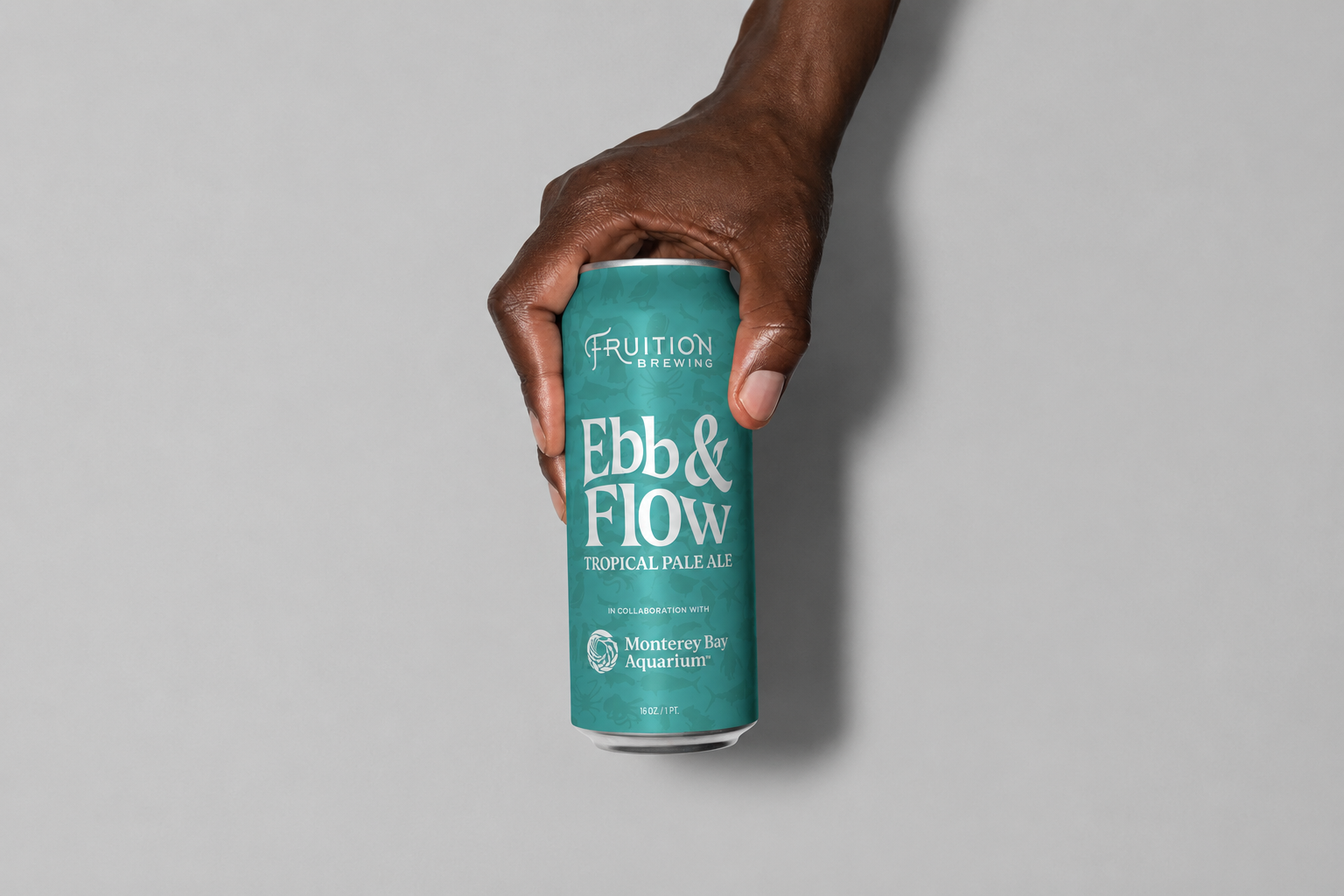 Hand holding a teal can of Fruition Brewing Ebb & Flow Tropical Pale Ale, created in collaboration with Monterey Bay Aquarium