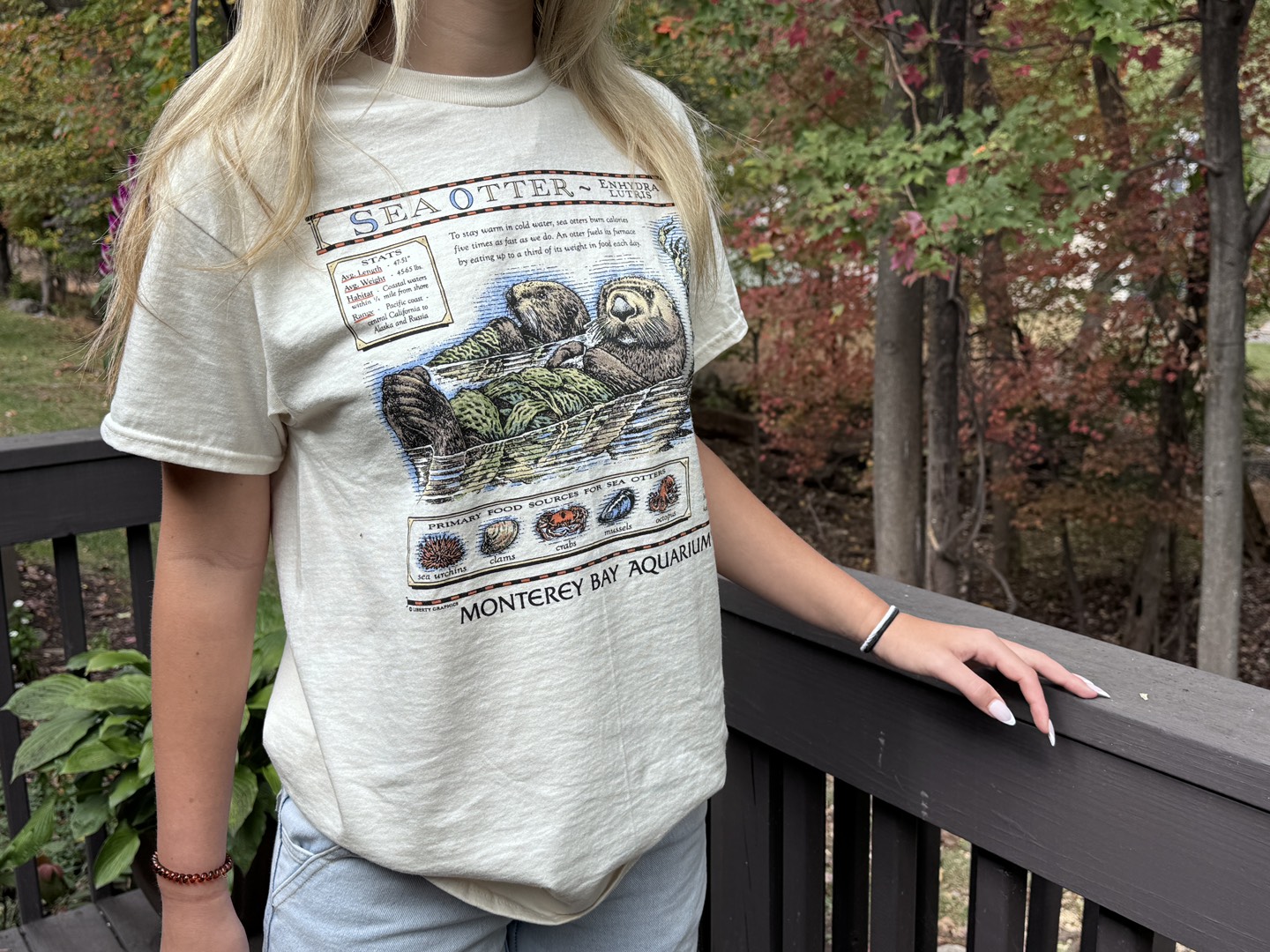 A person wearing the vintage sea otter tshirt outside with trees behind them