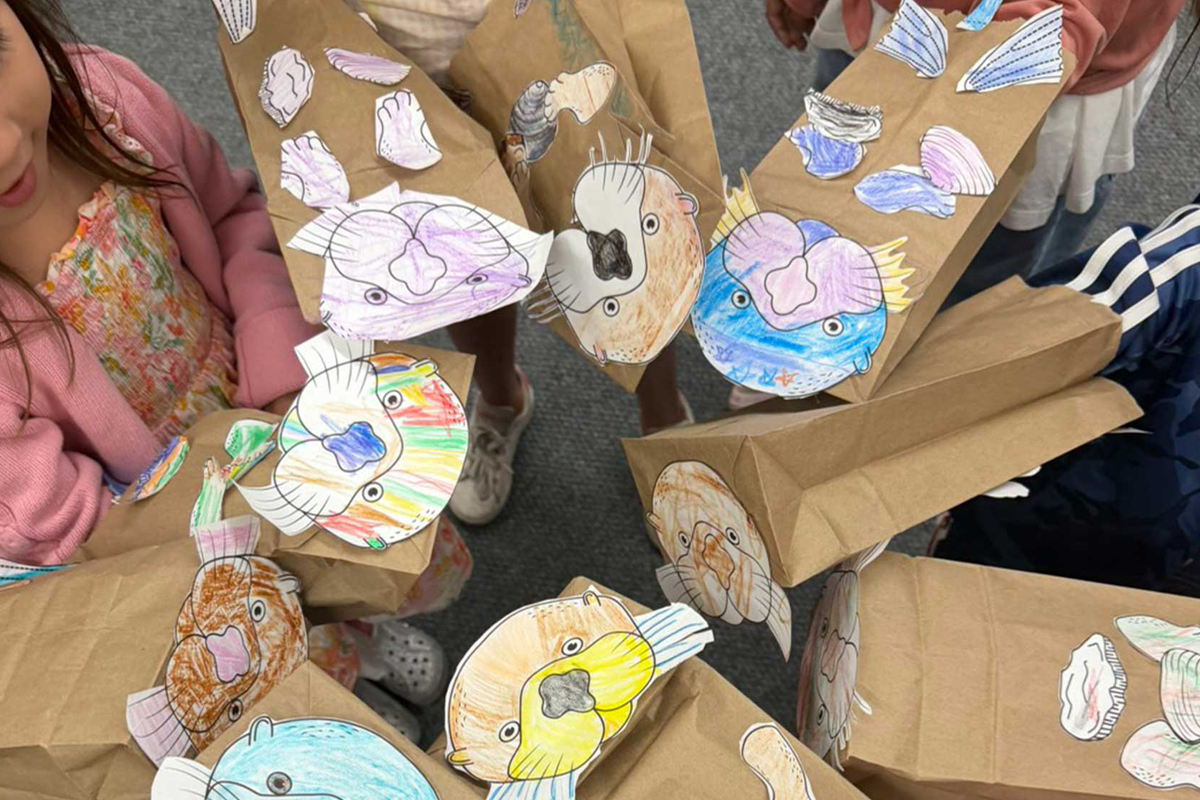 A group of students standing in a circle showing off their hand made otter puppets