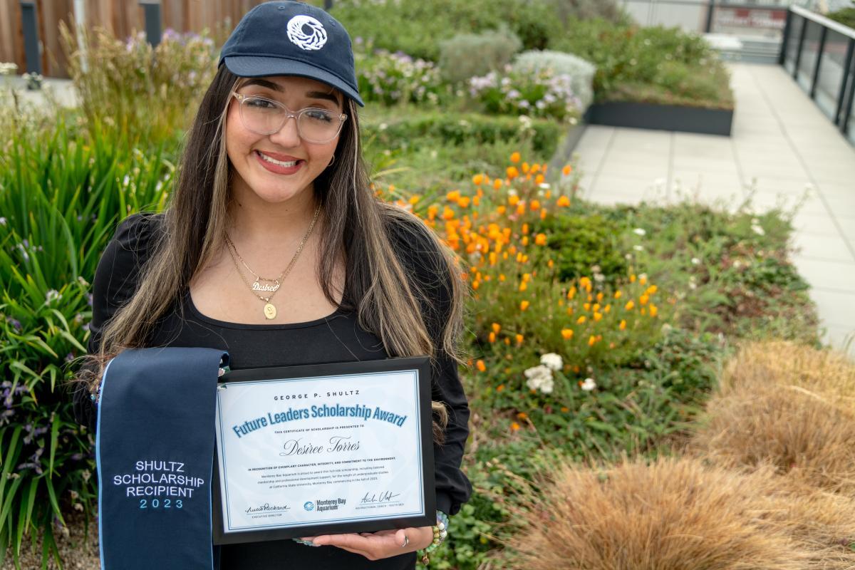 Scholarship recipient wearing a Monterey Bay Aquarium baseball cap and holding a sash and certificate for the Future Leaders Scholarship