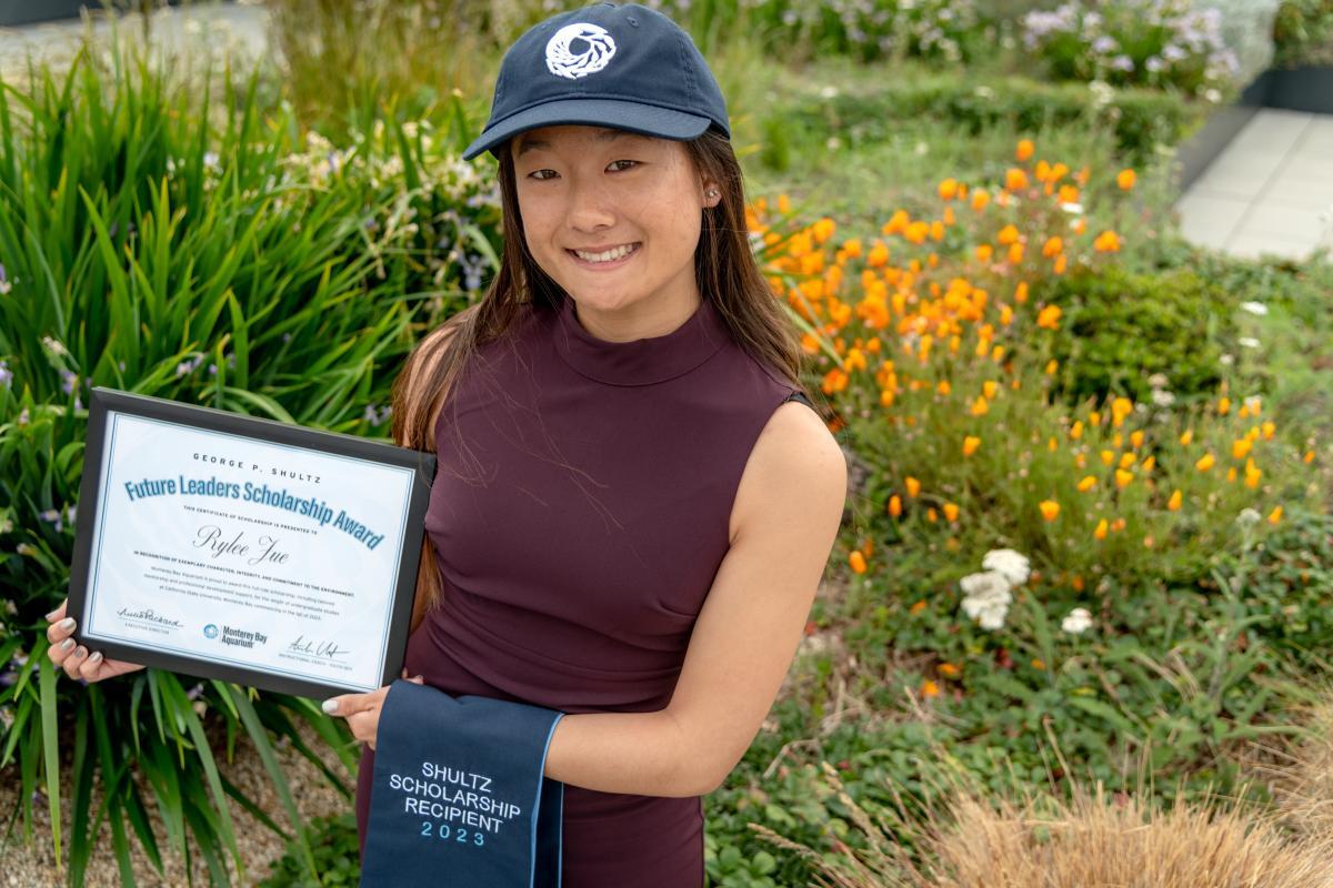 Scholarship recipient wearing a Monterey Bay Aquarium baseball cap and holding a sash and certificate for the Future Leaders Scholarship