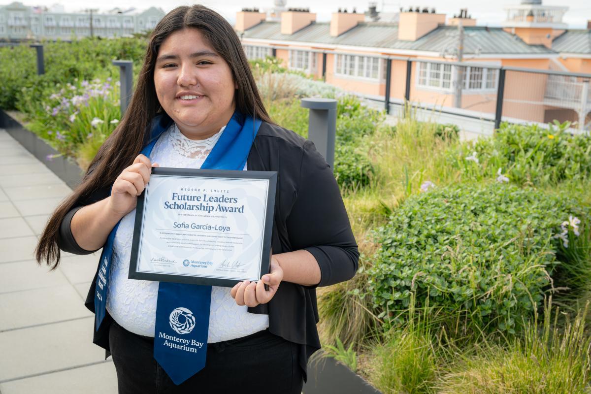 Scholarship recipient wearing a Monterey Bay Aquarium sash and holding a certificate for the Future Leaders Scholarship Award