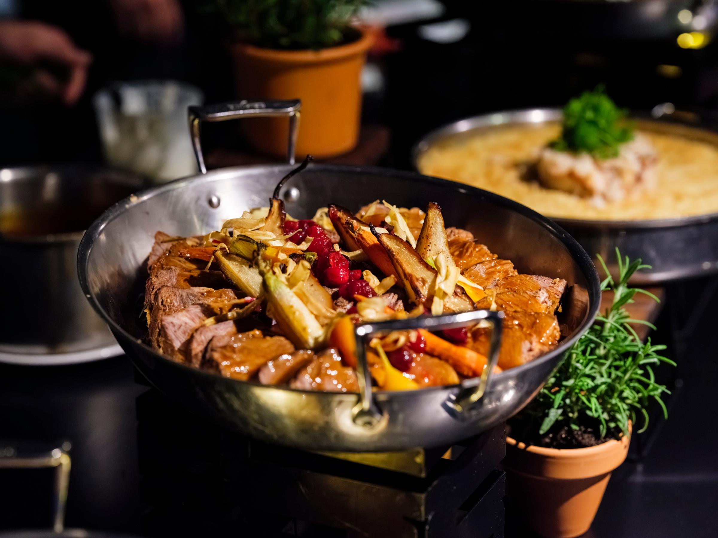 A metal serving bowl filled with a meat, vegetable, and fruit dish ready to be served to guests