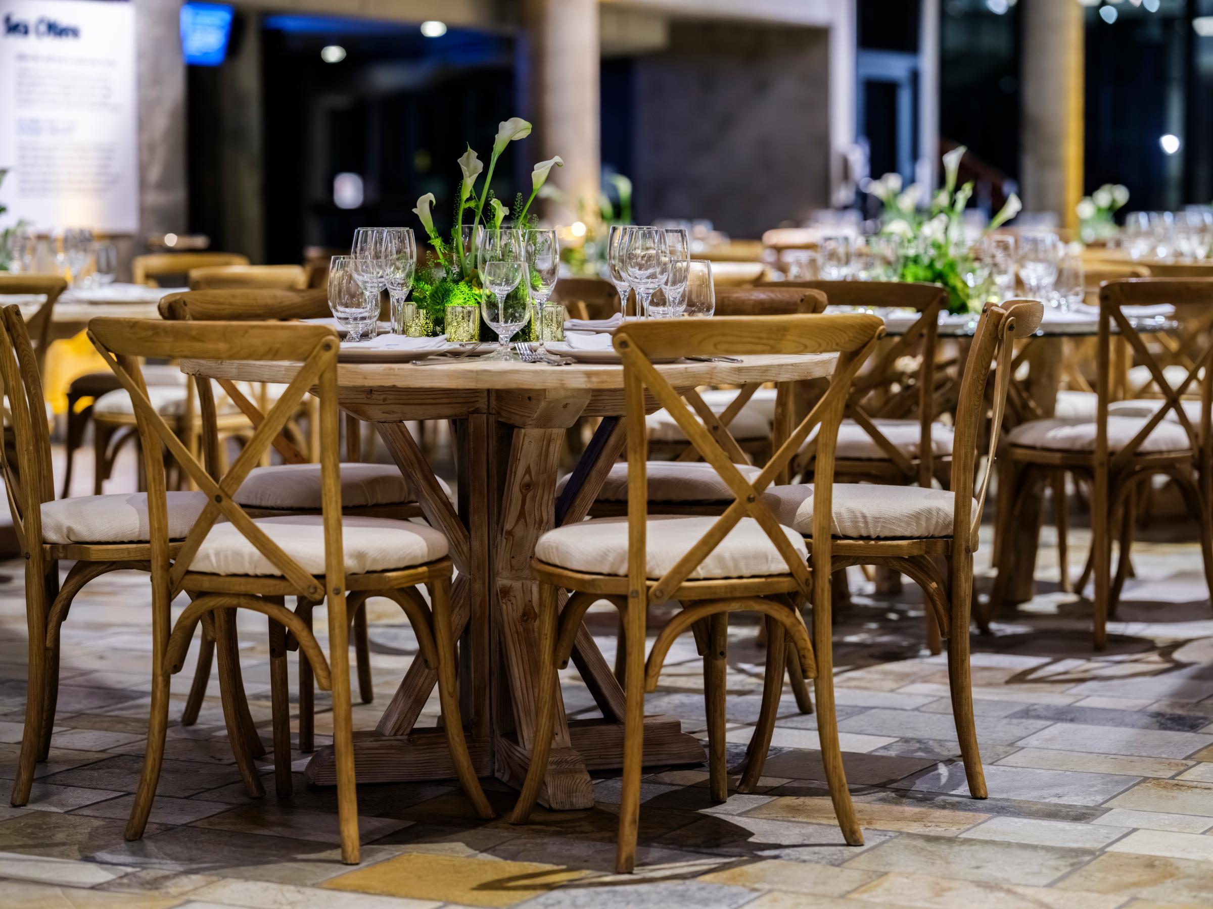 Chairs and tables made of light wood and set with glasses, plates, flowers, and other table setting items for an evening event in the Aquarium's marine mammal gallery