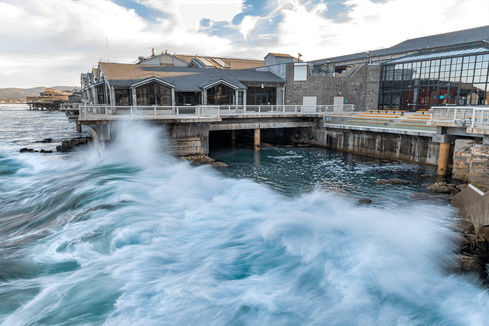 Large waves crashing against the base of the Aquarium building on a cloudy day
