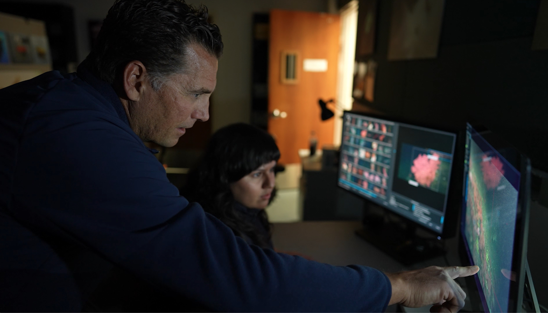 Two researchers stare at a video monitor showing live video feed from the deep.