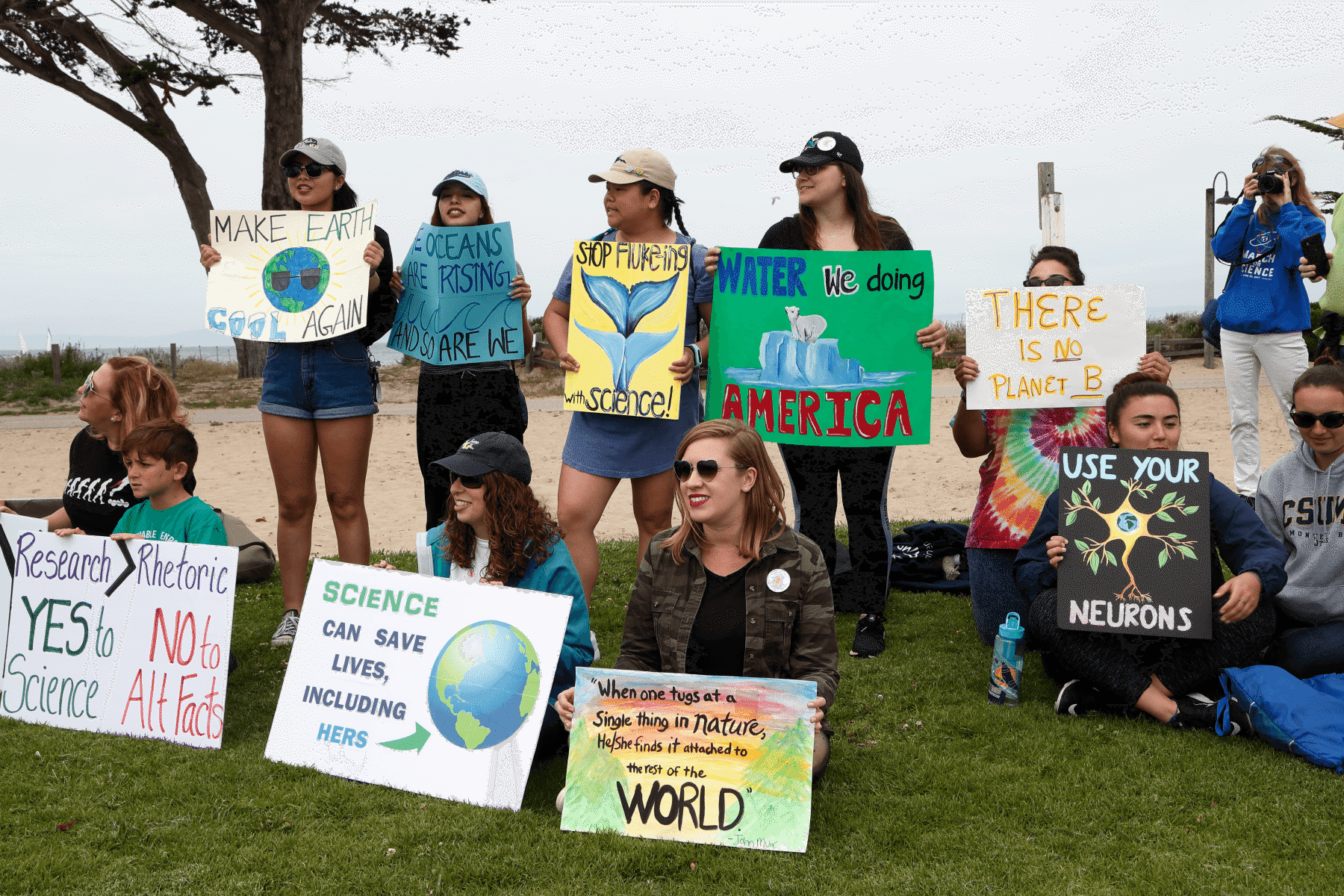 Group of people holding handmade science and climate advocacy signs at an outdoor rally near the beach
