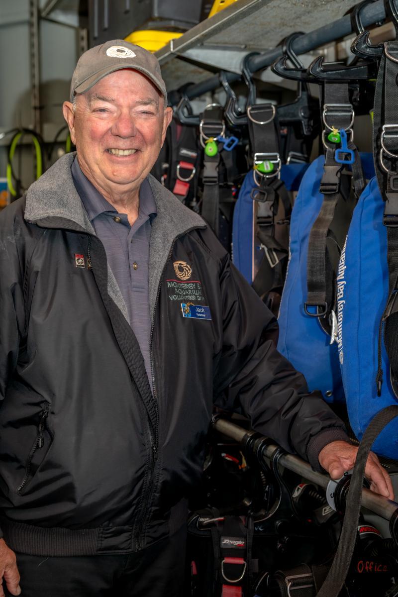 A volunteer smiles while standing next to diving gear
