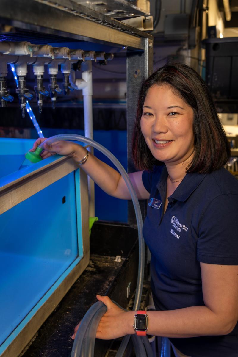 A volunteer smiles while holding a cleaning hose in a tank behind the scenes at the Aquarium