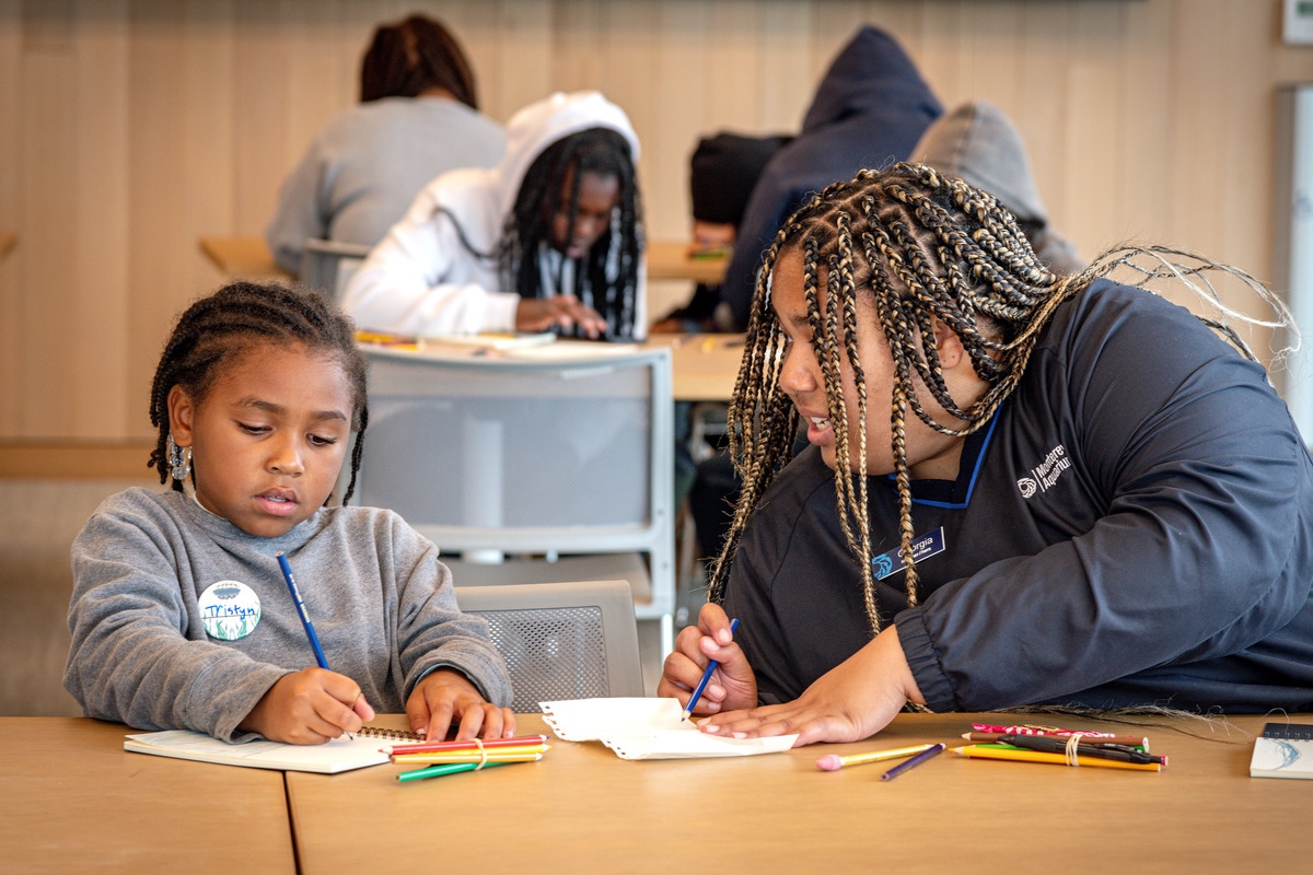 A staff member and a young student in the Bechtel Education Center working on some ocean work and other students in the background