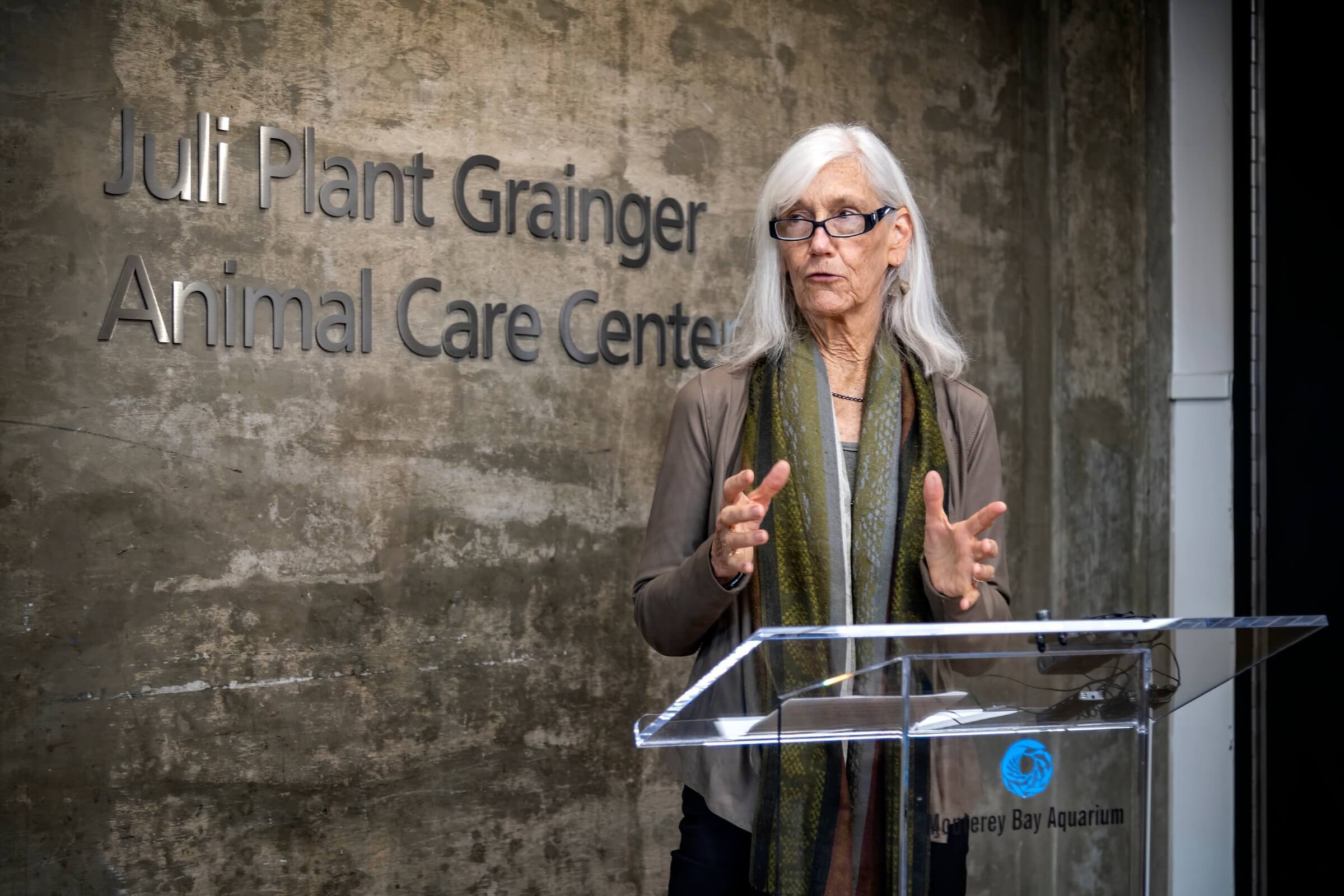 Julie Packard speaking at a podium in front of the Julie Plant Grainger Animal Care Center