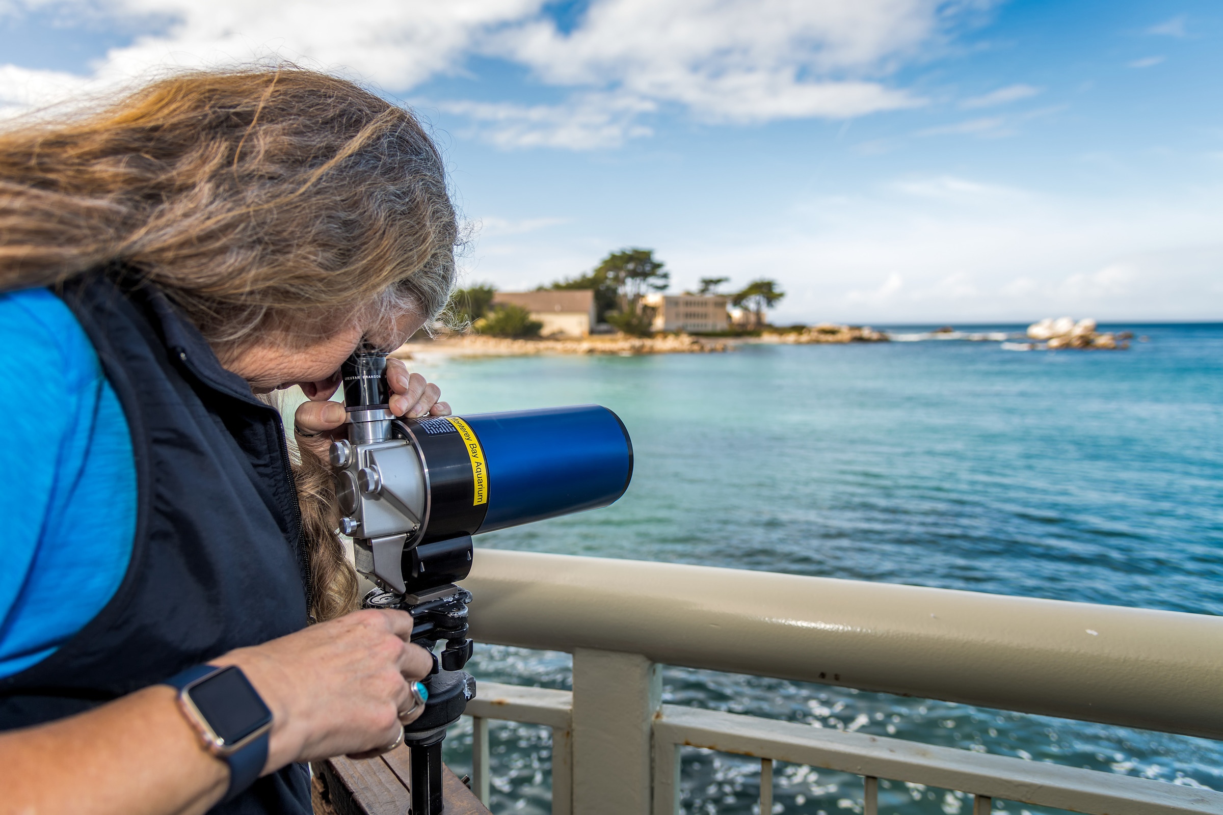 A staff member looking through a telescope searching for sea otters in the ocean behind them