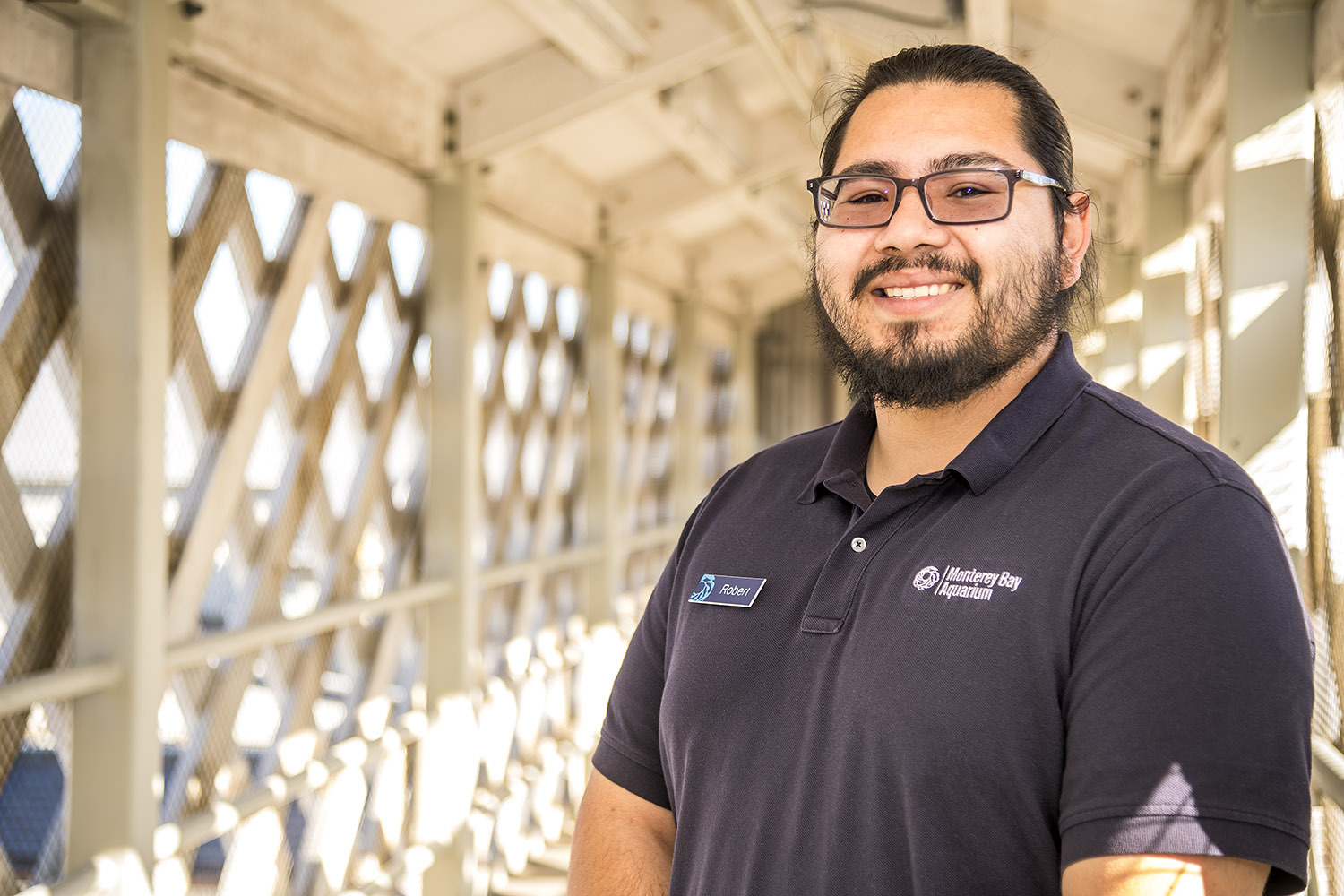 Roberto Flores wearing glasses and an Aquarium uniform collared shirt standing on a bridge