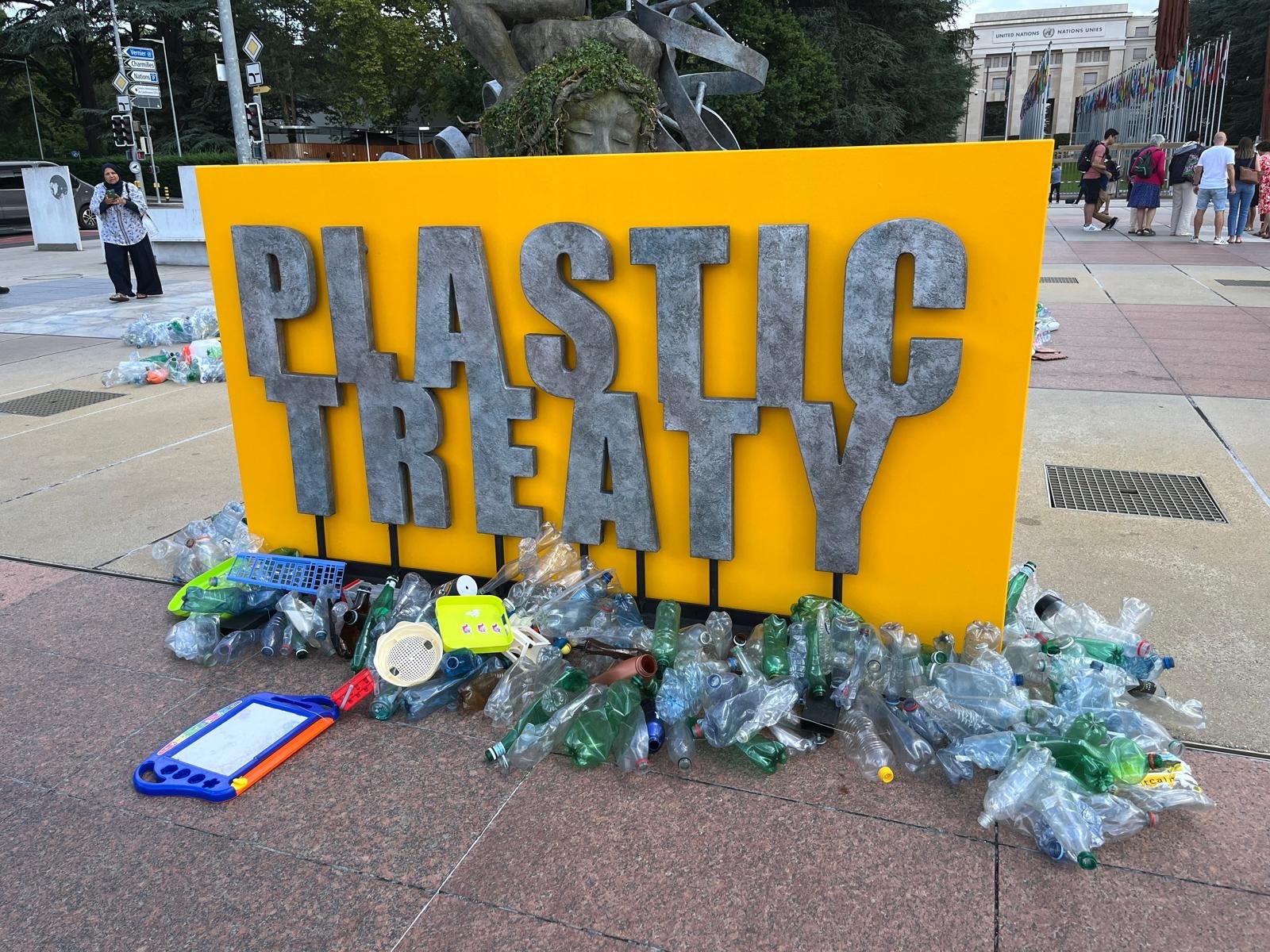 Large yellow sign with plastic treaty written on it in front of plastic trash.