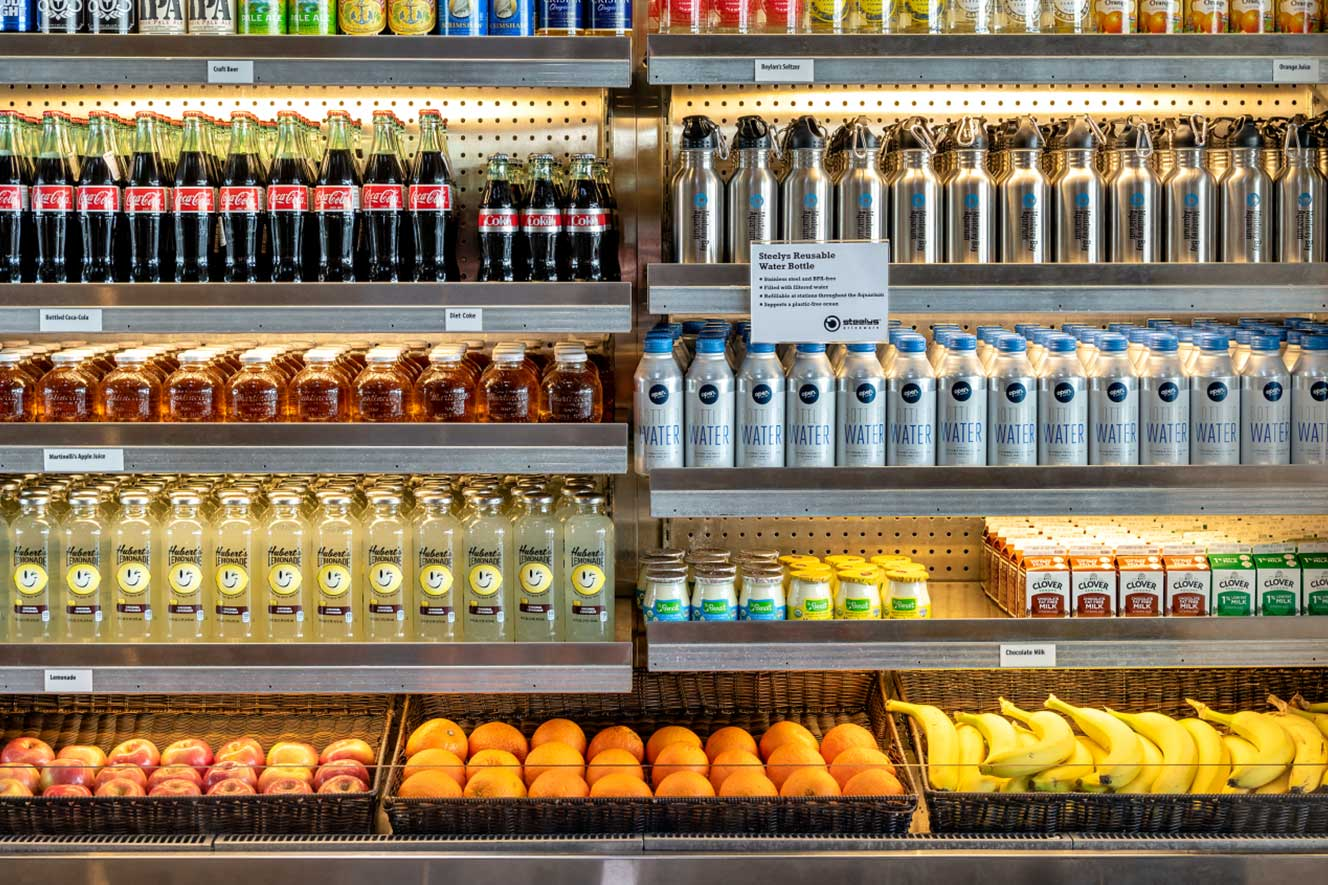 Refrigerated display case stocked with beverages, reusable water bottles, and fresh fruit at the Aquarium