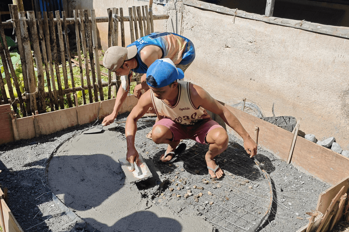Two people setting cement on foundation for a rainwater collection system