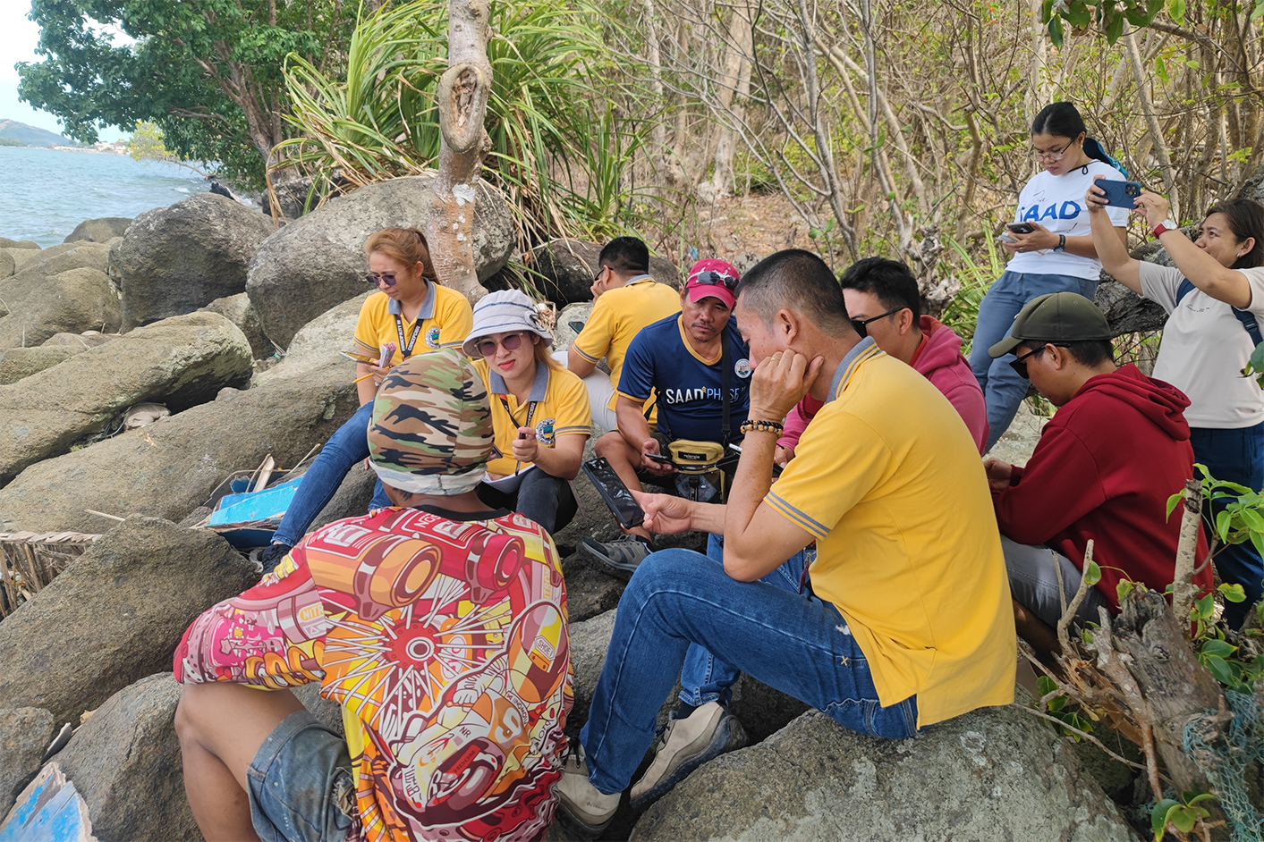 Group of people in yellow shirts sit on coastal rocks during an outdoor training session in the Philippines