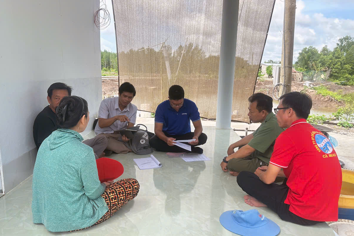 Six people seated in circle on floor reviewing documents at Vietnamese shrimp farm