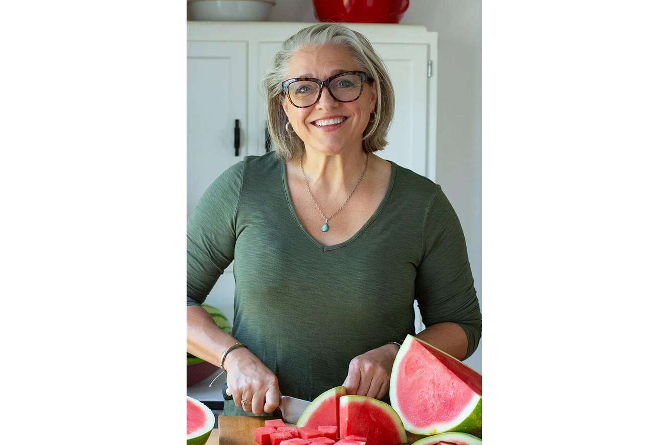 Chef Willis standing cutting watermelon wearing a green long sleeve shirt and black rimmed glasses