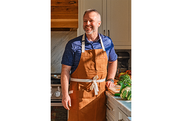 Photo of William Dissen wearing a brown apron, standing in a kitchen.