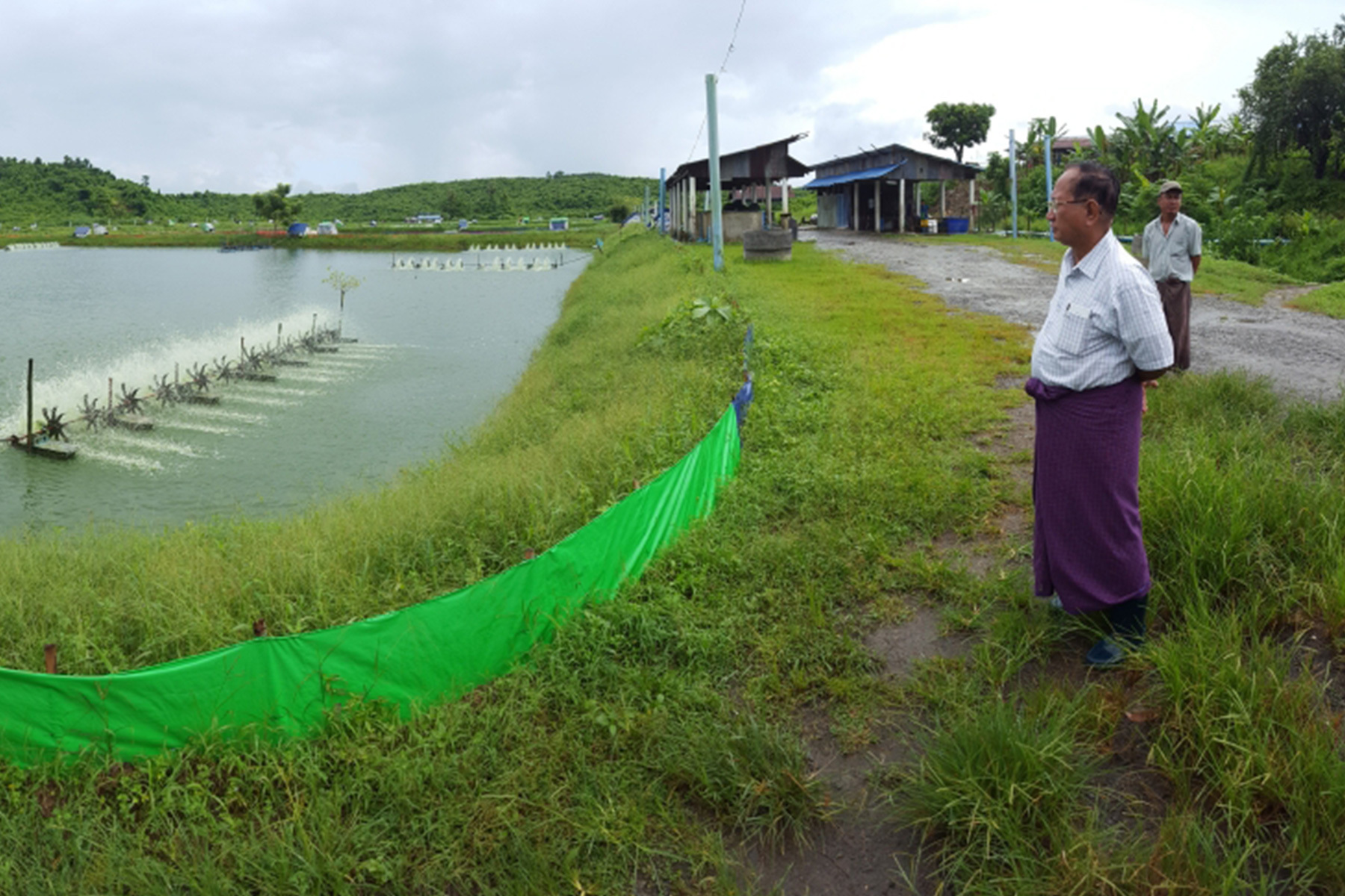 A man in Vietnam stands right of a small body of water that is used for sustainable fish farming