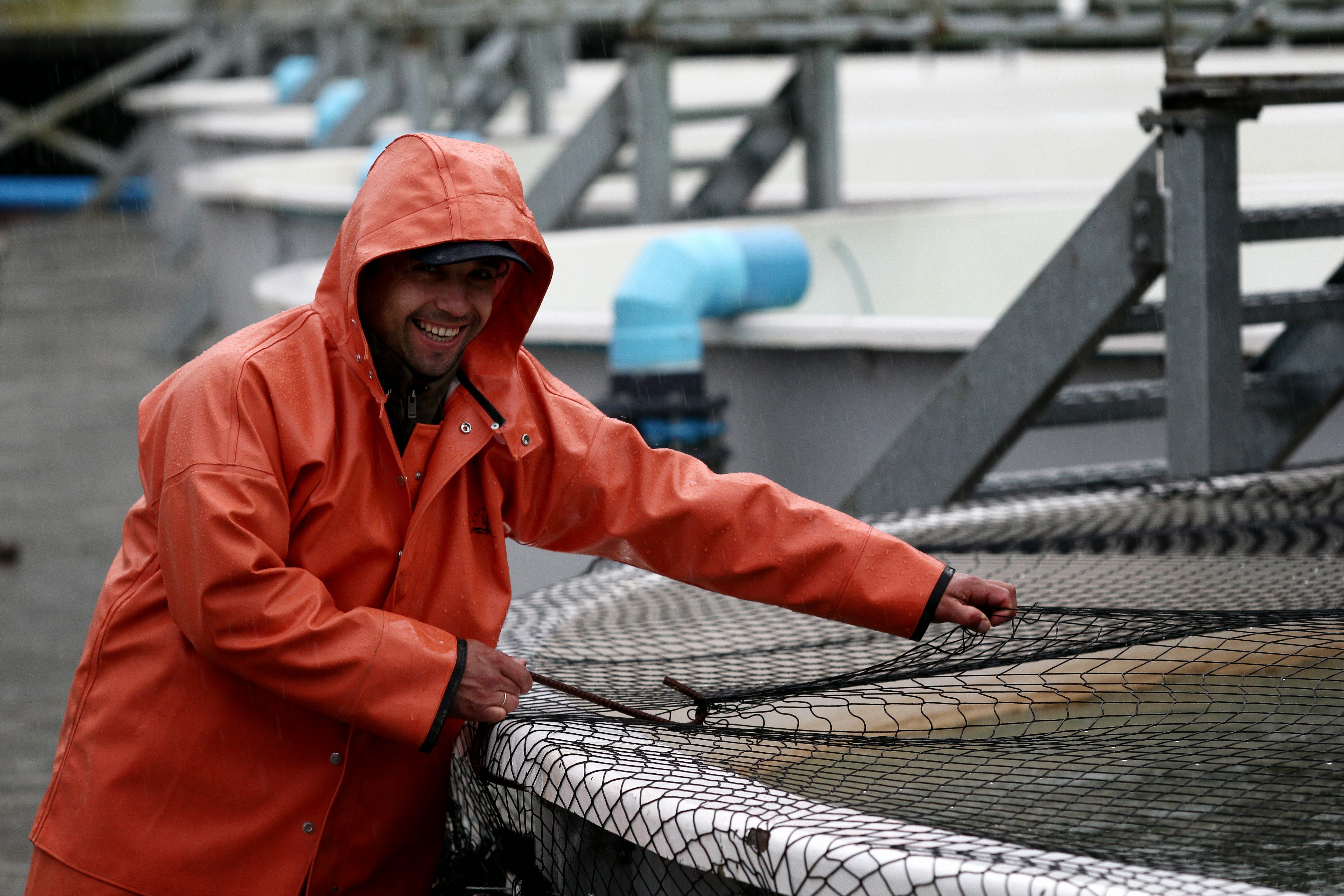 A fisherman in an orange raincoat with the hood up holding onto a large net on a fishing dock