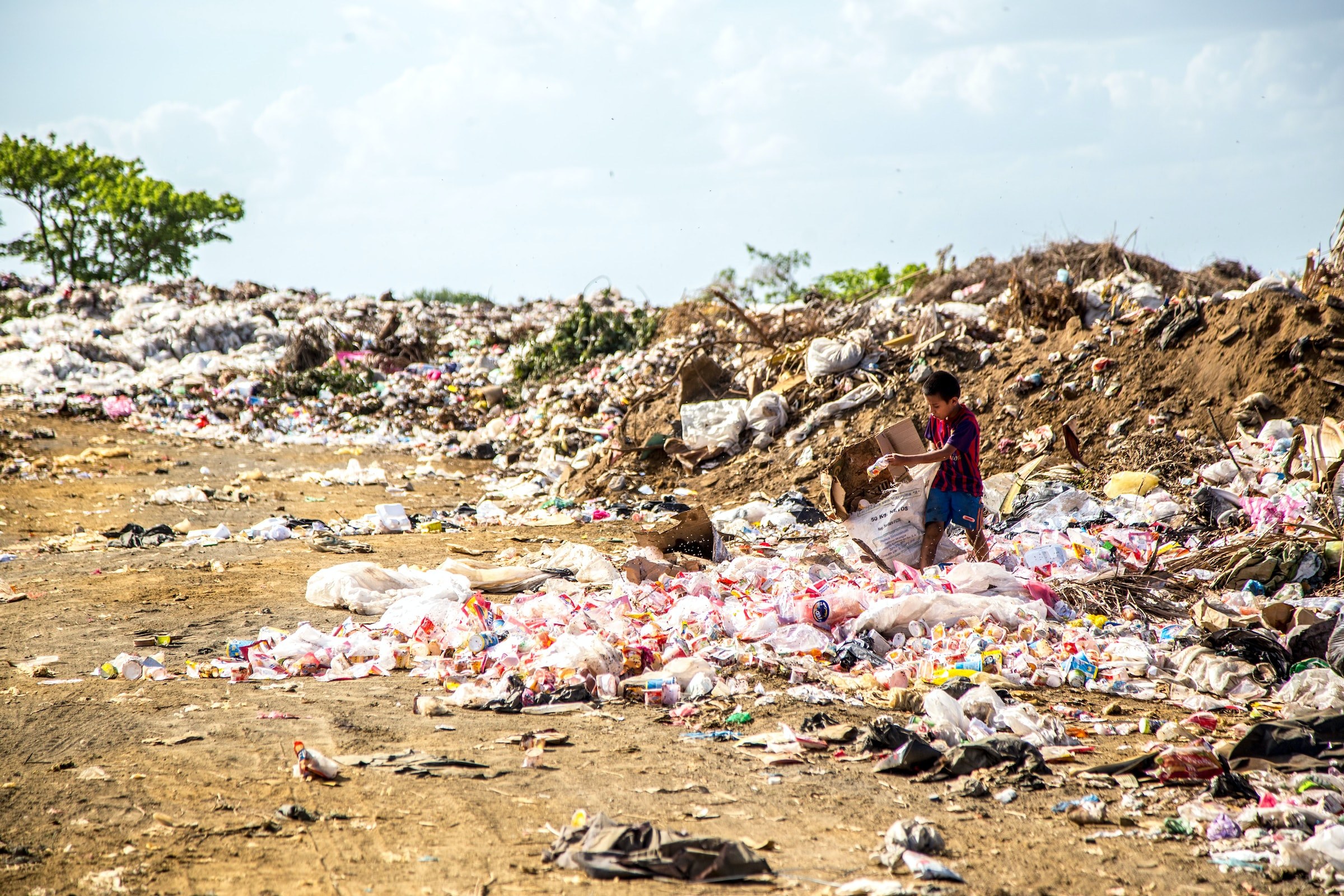 A young boy standing on top of garbage dump picking through trash items in Nicaragua.