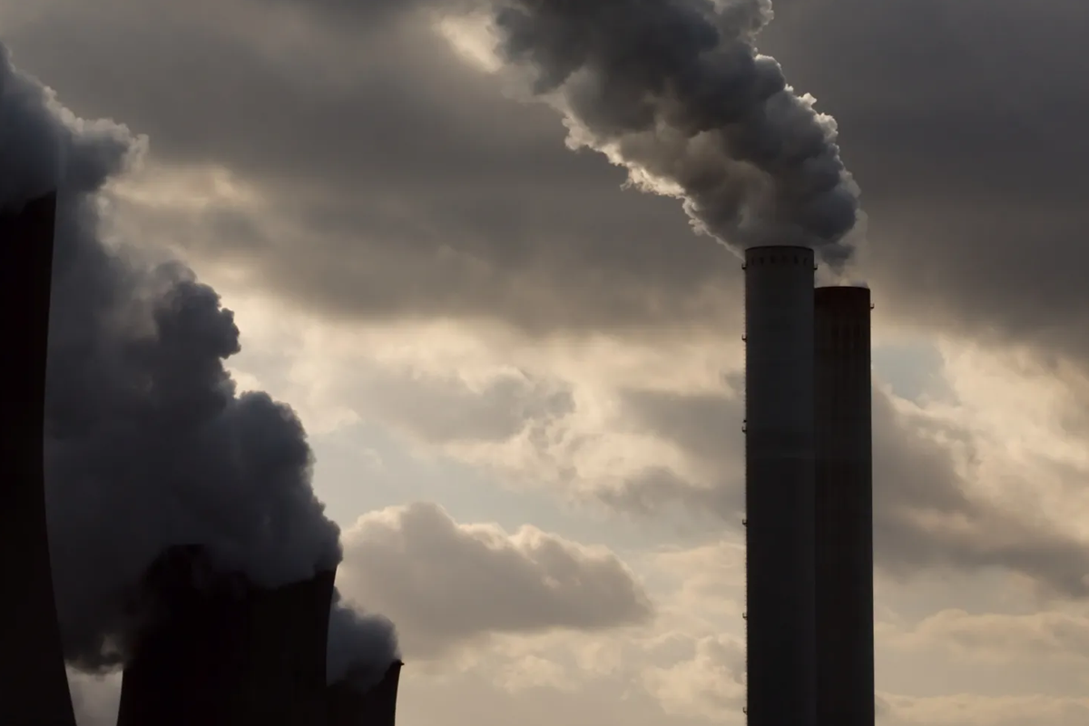 Industrial smokestacks emitting large plumes of smoke against a cloudy and overcast gray sky