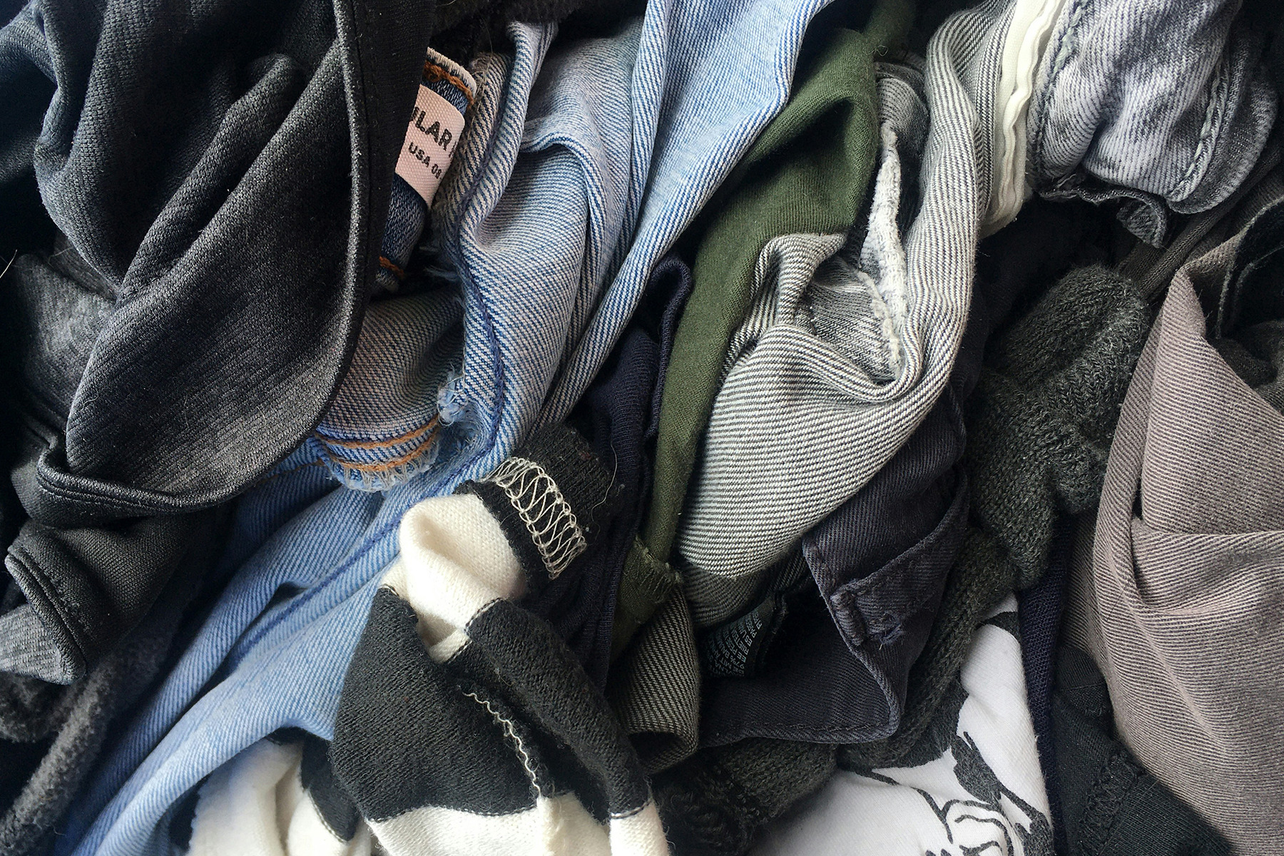 Pile of mixed clothing including jeans and dark garments, representing textile waste