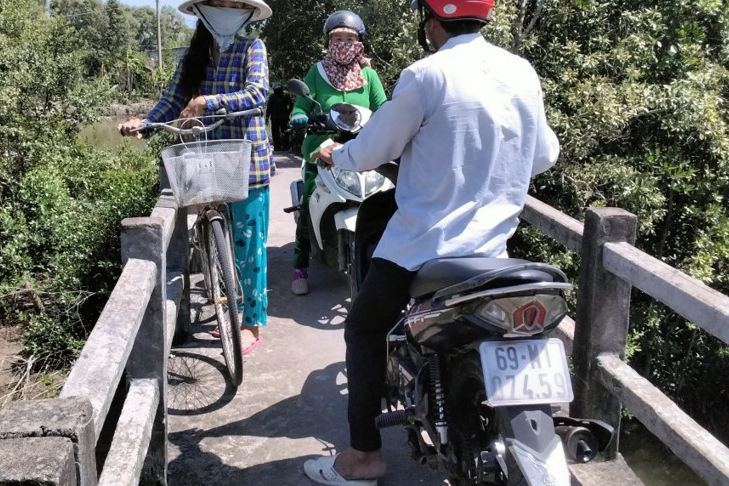 Several people struggling through traffic on an old narrow bridge in Vietnam