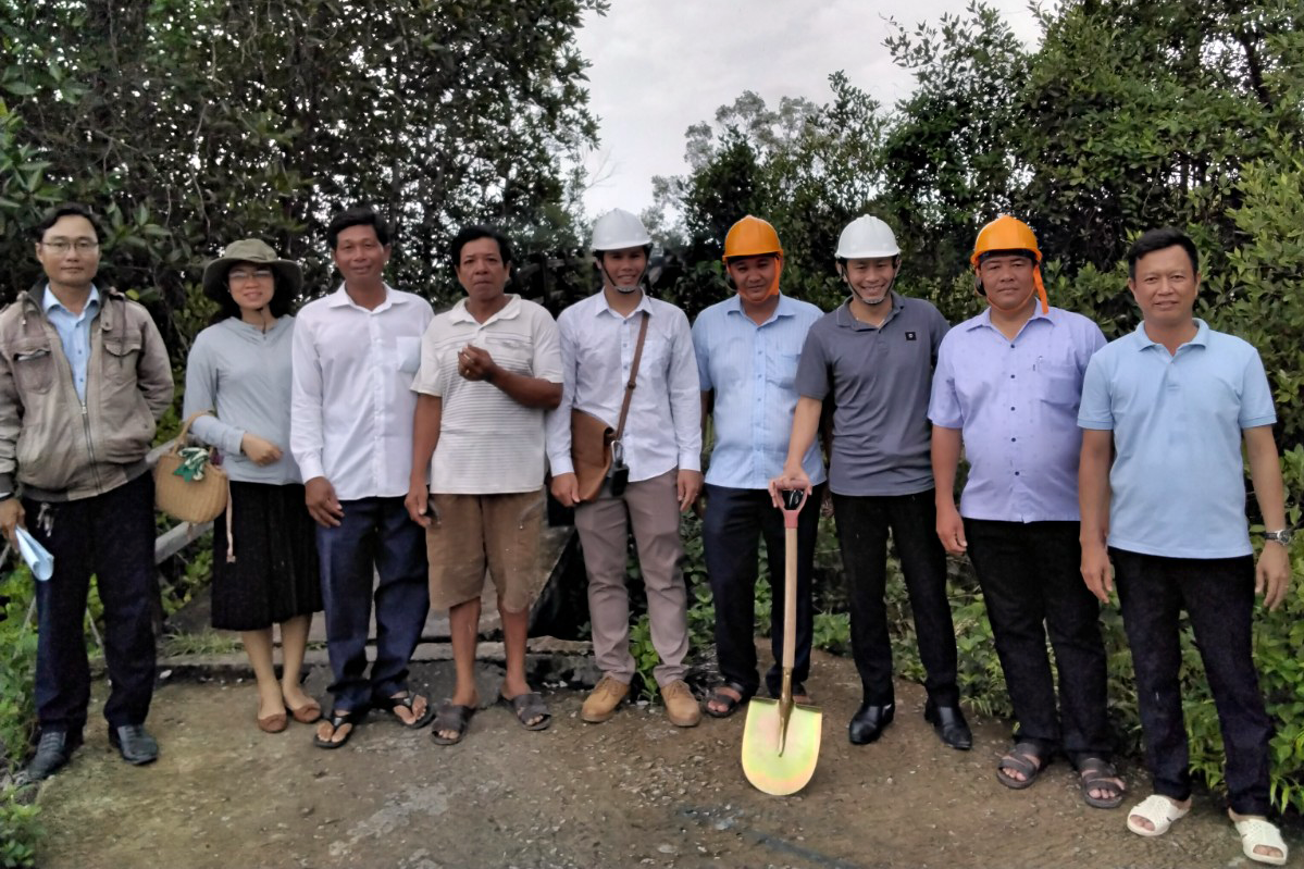 Community leaders and officials in hard hats pose with a shovel at a mangrove forest groundbreaking ceremony