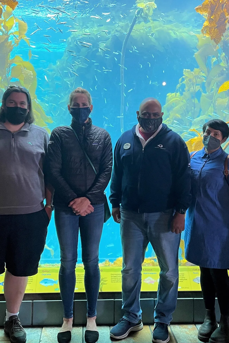 A group of aquarium colleagues standing in front of kelp forest at the Aquarium