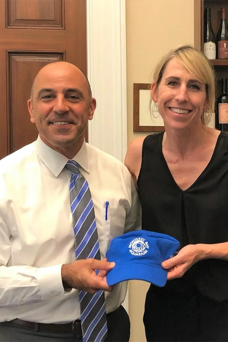 Eleanore standing with U.S. Representative Jimmy Panetta in his office holding a Monterey Bay Aquarium branded cap.