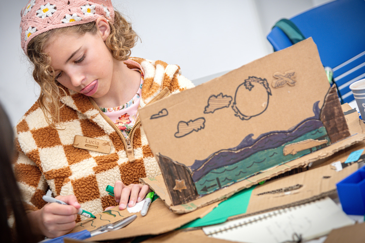 A blond teenager in a colorful outfit working on an engineering project with a focused expression