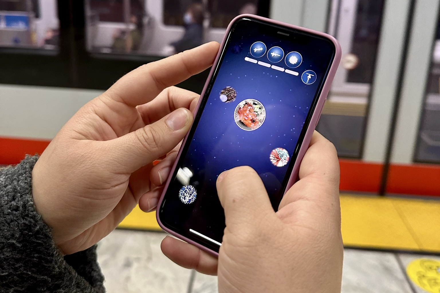 A pair of hands hold a smart phone, the screen displays the FathomVerse game.