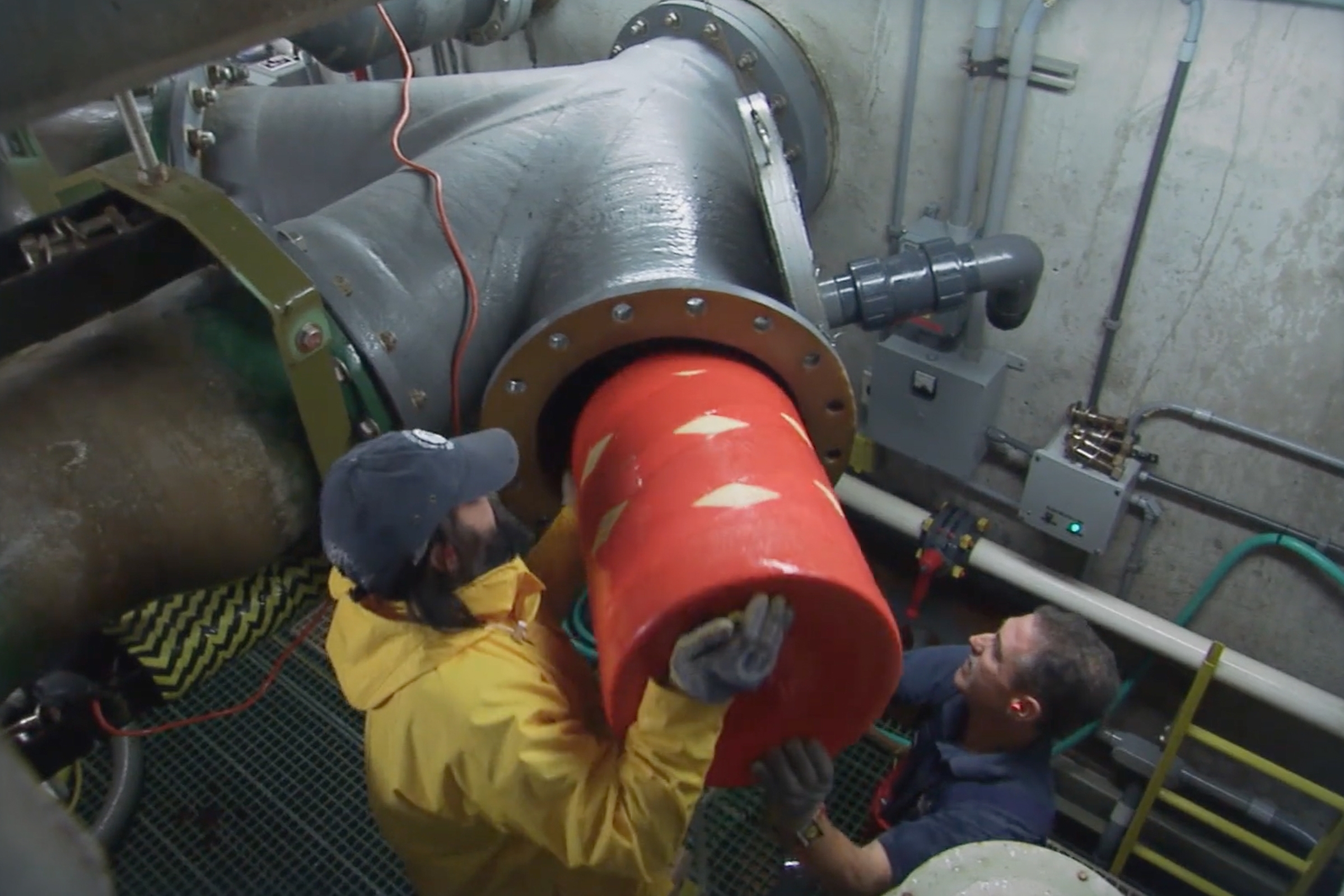 Two Aquarium staff placing the red cylinder pig into the pipes