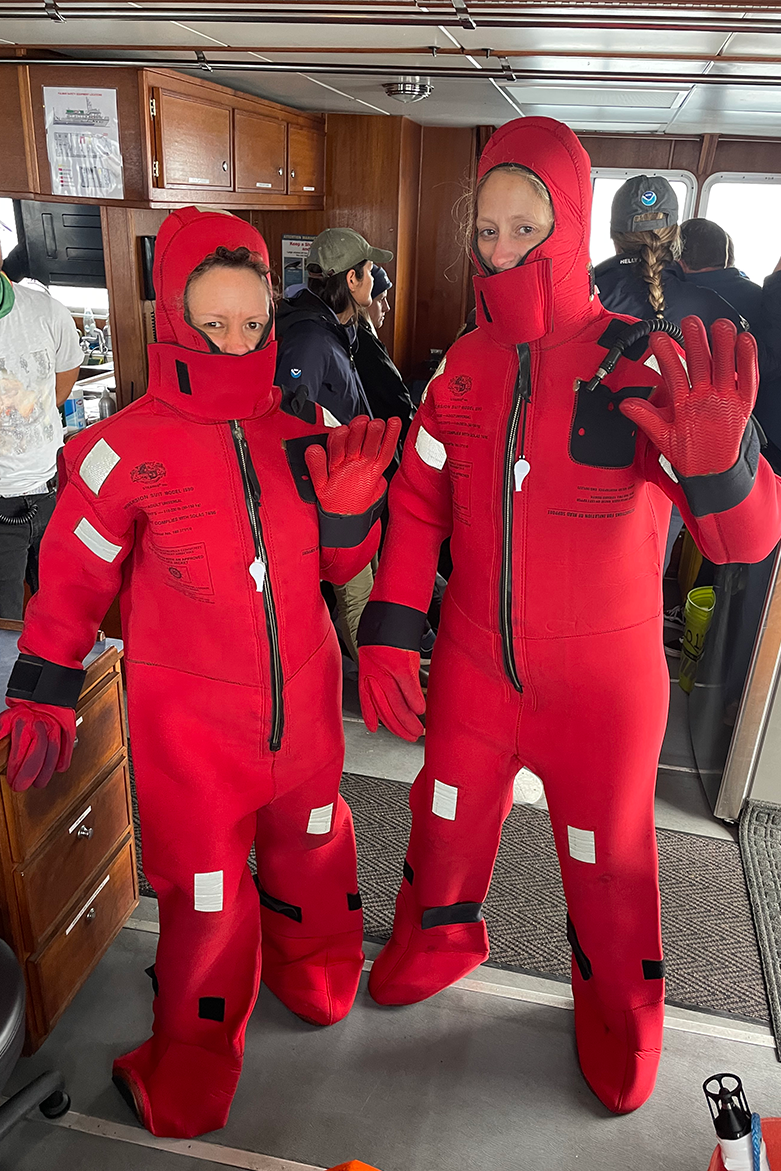Two women dressed in puffy, bright red, full body survival suits.