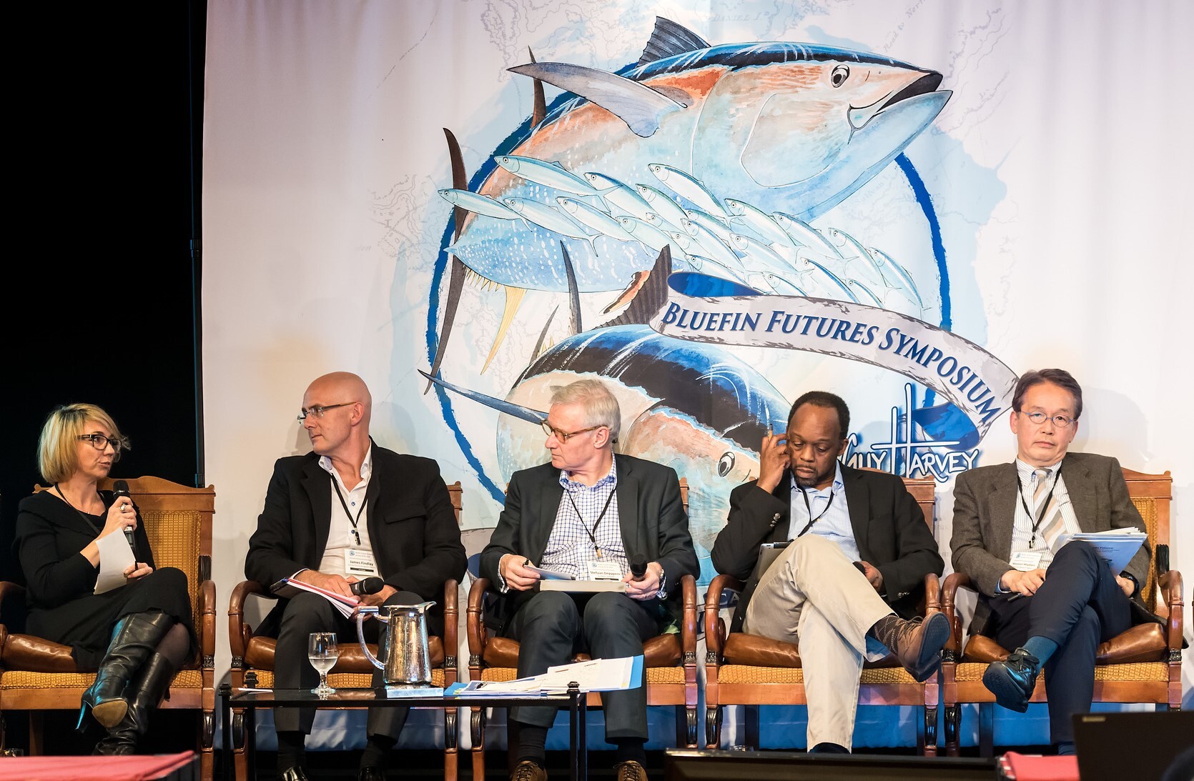 Five panelists seated on stage at the Bluefin Futures Symposium. Behind them is a large mural of a tuna, creating a focused and serious tone